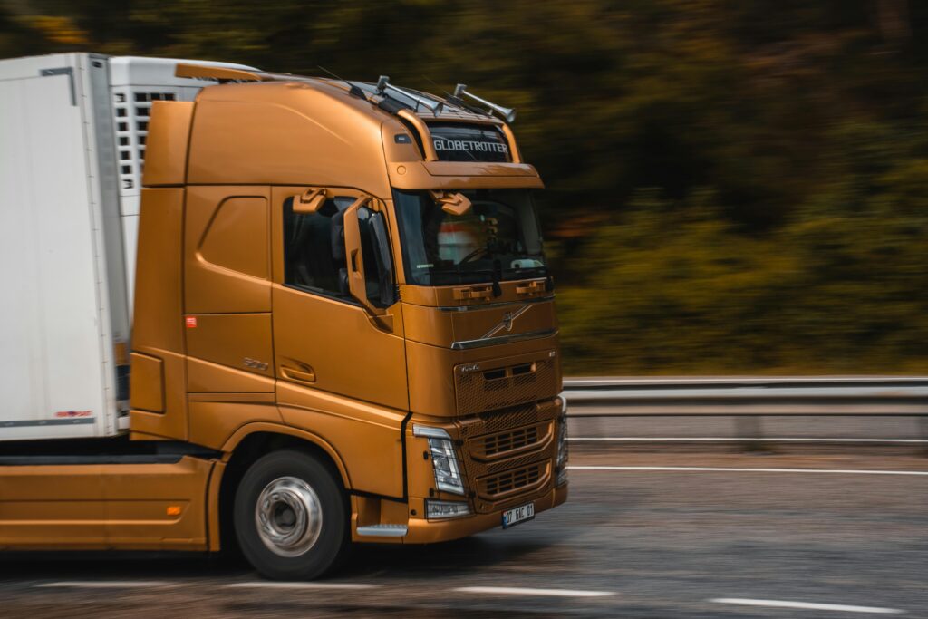 pexels-photo-16706765-16706765 Orange truck speeding along a highway in Kemer, showcasing transportation and logistics.